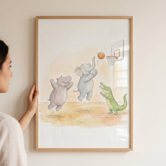 Person holds framed watercolor basketball safari animals wall art of a hippo, elephant, and crocodile.
