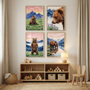 A set of four watercolor-style illustrations featuring brown bears is displayed on a light-colored wall. Each artwork is set in a simple wooden frame and arranged in a grid pattern. The scenes depict bears in various natural settings: one sits peacefully in a flowered meadow, another is shown in a close-up portrait, a third stands tall in a grassy field, and the last drinks from a mountain lake. All pieces share a soft color palette of blues, pinks, and earth tones.

