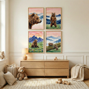 A light-filled nursery features four framed watercolor-style illustrations of brown bears in mountain landscapes. The art shows a bear's profile, one standing, one sitting in flowers, and two on a log. Below, a light wood dresser holds a small lamp and wooden blocks. On a textured rug, a large soft plush bear sits by a basket and pillows. A wooden toy car and another basket with a blanket complete the cozy room. The walls are a neutral off-white with classic molding.