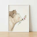 A whimsical watercolor-style illustration features two bears. A large, cream-colored bear holds a pink flower by its stem in its mouth. A smaller brown bear cub rests comfortably on the larger bear's back. A delicate yellow butterfly is near the pink flower. The artwork is showcased in a slim white frame, which sits on a light-colored wooden surface against a plain white wall.