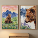 Two rectangular framed artworks hang side-by-side on a neutral wall. Each features a brown bear in a serene natural setting, rendered in a soft watercolor style. The piece on the left shows a full-bodied bear sitting in a vibrant green meadow dotted with small, colorful wildflowers, set before jagged blue mountains under a warm pink and orange sky. The piece on the right displays a close-up profile of a bear's head, gazing down at a patch of purple and blue flowers, with faint blue mountains.