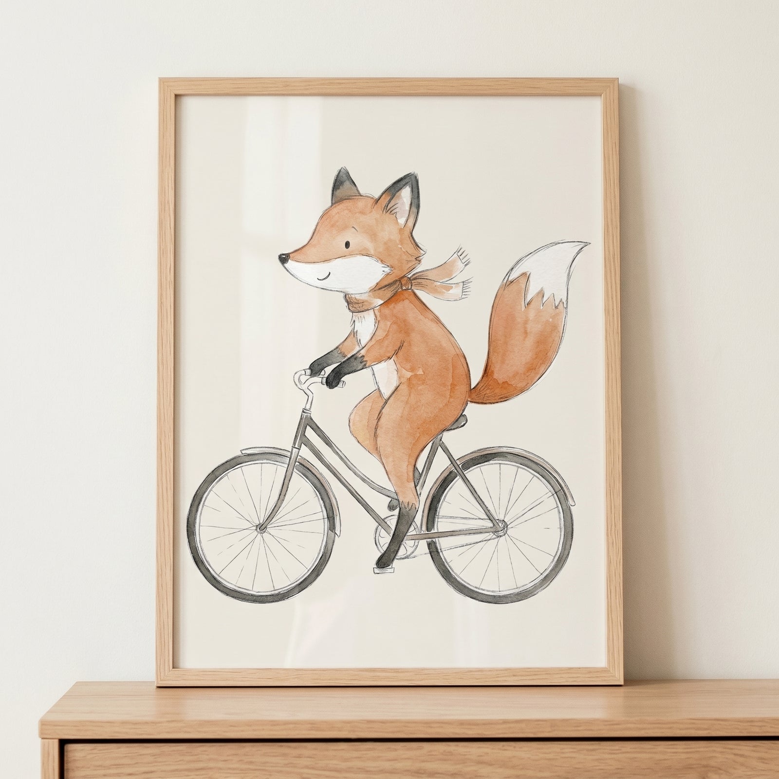 Watercolor bicycle riding fox wall art in a wooden frame shows an orange fox with a scarf on a grey bike.