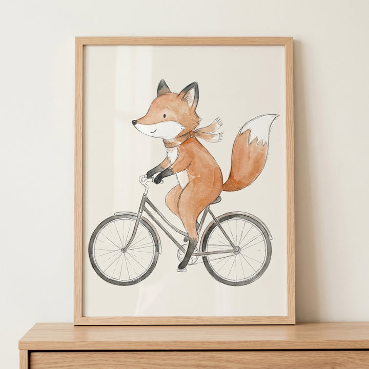 Watercolor bicycle riding fox wall art in a wooden frame shows an orange fox with a scarf on a grey bike.
