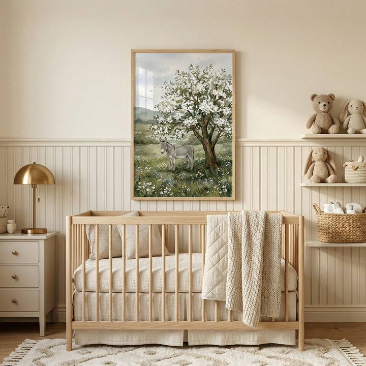 A serene, neutral-toned nursery features a light wood crib with soft cream bedding and a textured throw blanket. Above the crib hangs a large framed art print of a donkey standing in a lush green field filled with white flowers, positioned beneath a large tree covered in white blossoms. 