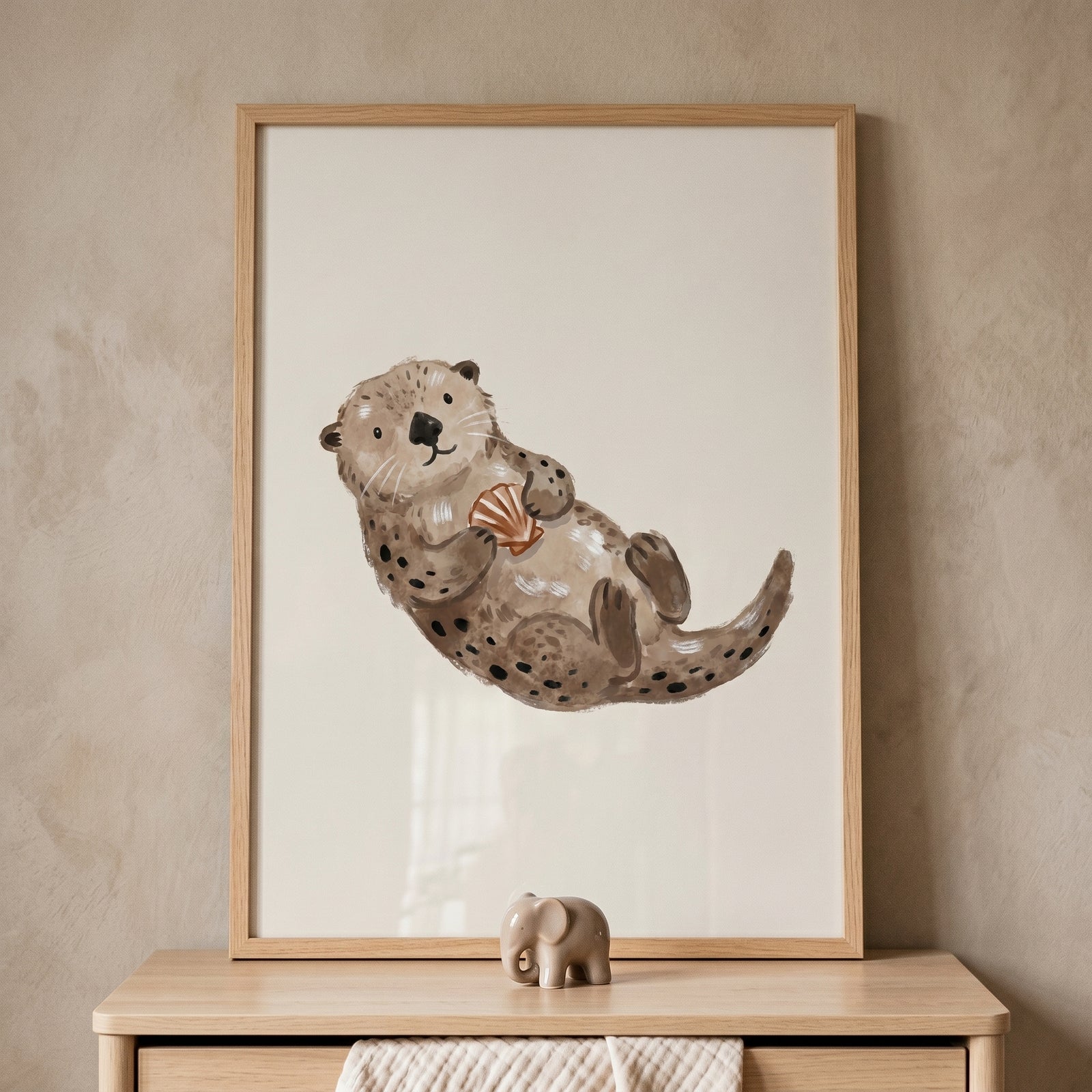 Framed watercolor brown sea otter wall art of a sea otter holding a shell above a wooden dresser.