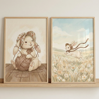 Two framed watercolor illustrations sit side-by-side on a light-colored wooden shelf. The left illustration features a charming bunny wearing a floral-patterned hat, sitting on a wooden surface and holding a large ball of yarn. The right illustration shows a similar bunny leaping through a sunlit field of wildflowers, wearing a bonnet with long, flowing ribbons. Both pieces share a soft, whimsical style with warm, neutral tones and are housed in minimalist wooden frames.