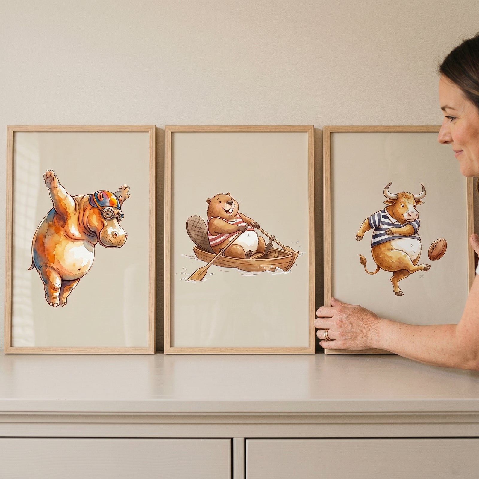 Watercolor competitive athletic animals wall art set of 3 with a diving hippo, rowing beaver, and a bull playing football.