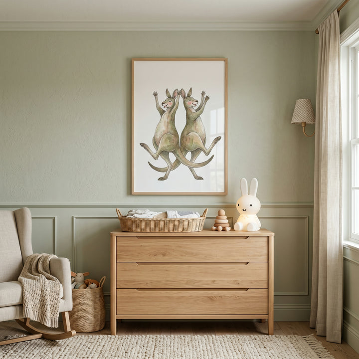 Watercolor dancing kangaroo wall art over a wood dresser in a green nursery with a rabbit lamp and rocking chair.