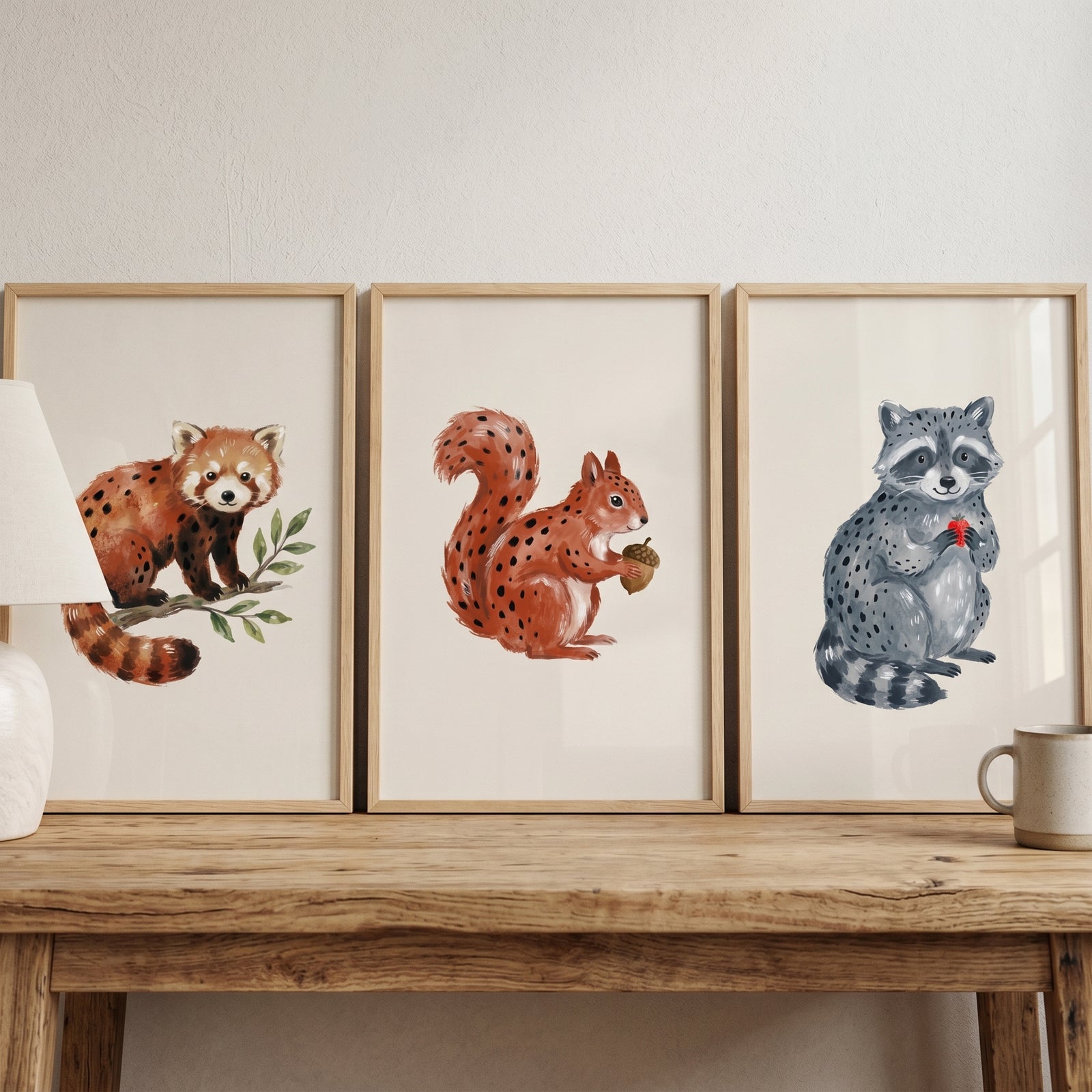 Watercolor earthy woodland animals wall art set of 3 featuring a red panda, squirrel, and raccoon on a wooden table.