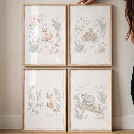 Four light wood frames display a watercolor fairytale forest animal wall art set of 4 on a white wall.