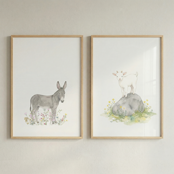 Two vertical light wood frames hang side-by-side on a neutral wall. Each frame holds a watercolor-style illustration of a baby animal on a white background. The frame on the left depicts a grey donkey foal standing in a bed of pastel-colored wildflowers. The frame on the right depicts a small white goat standing atop a smooth grey stone, which is nestled among green grass and yellow blossoms. The artwork has a soft, whimsical feel, suitable for a nursery.