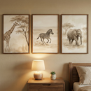 Three framed pieces of artwork featuring safari animals are hung in a row on a soft beige wall above a nightstand. From left to right, the illustrations depict a giraffe standing beside a tree, a zebra running through an open landscape, and an elephant walking through tall grass. All three images share a muted, sepia-toned watercolor-like style with a color palette of tan, cream, and brown.
