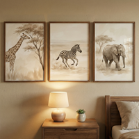 Three framed pieces of artwork featuring safari animals are hung in a row on a soft beige wall above a nightstand. From left to right, the illustrations depict a giraffe standing beside a tree, a zebra running through an open landscape, and an elephant walking through tall grass. All three images share a muted, sepia-toned watercolor-like style with a color palette of tan, cream, and brown.
