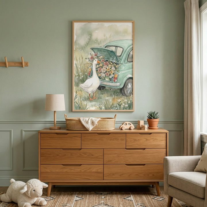 A serene nursery interior features a vertical wooden-framed illustration centered on a sage green wall. The artwork depicts a whimsical scene with a white goose standing in a field of wildflowers next to a small, light green vintage-style car. The car's trunk is open and brimming with a vibrant bouquet of flowers in shades of pink, yellow, and red, rendered in a soft, watercolor-like style.
