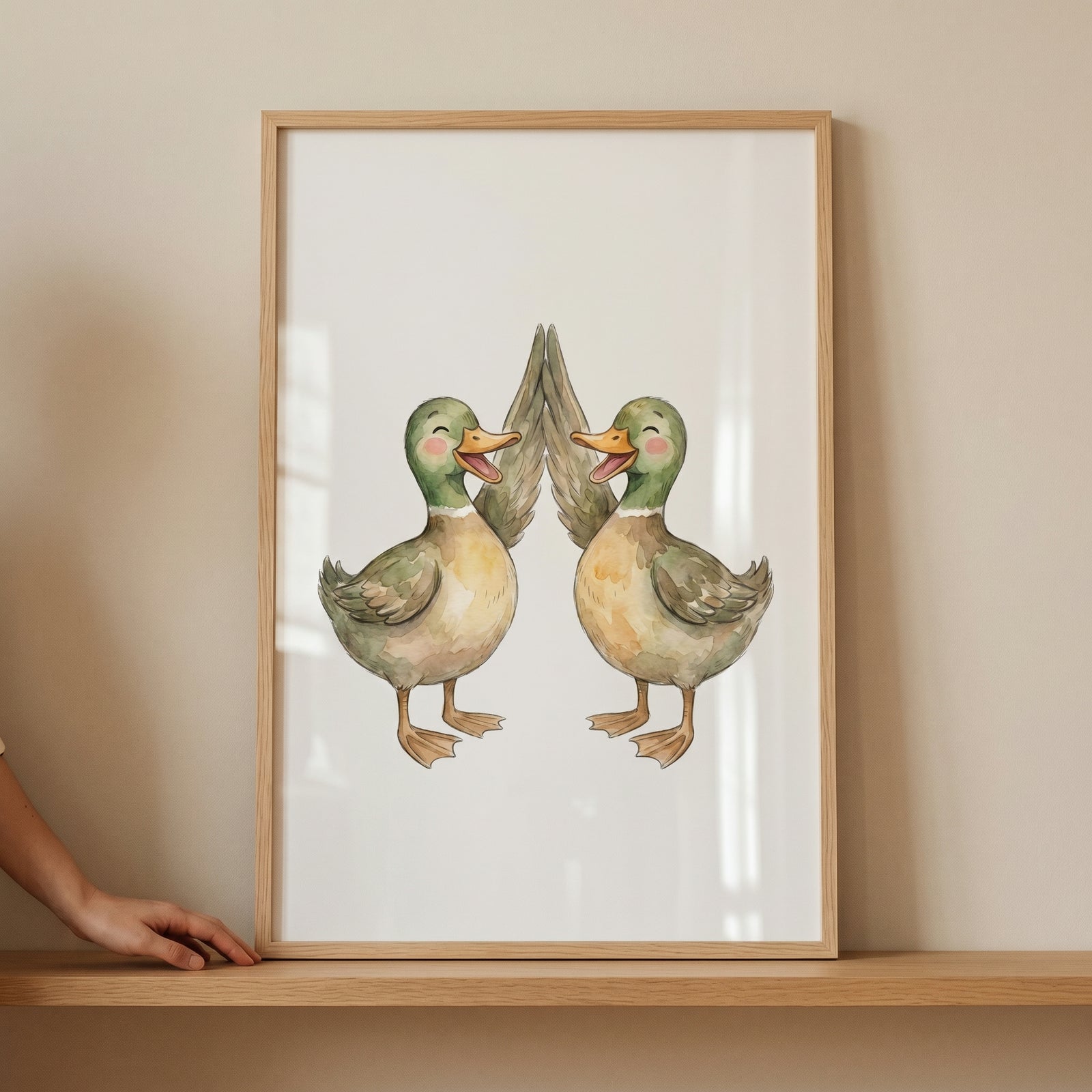 Watercolor high five ducks wall art shows two smiling ducks high-fiving in a thin wooden frame on a light shelf.