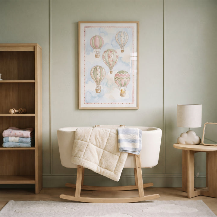 Sage green nursery with watercolor hot air balloon wall art above a white rocking bassinet and light wood furniture.