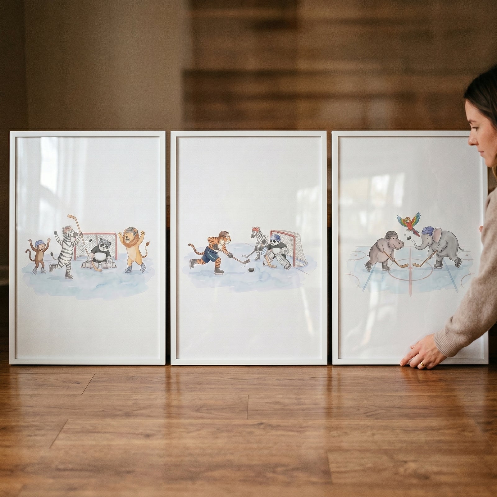 A woman touches a watercolor ice hockey animals wall art set of 3 in white frames resting on a wooden floor.