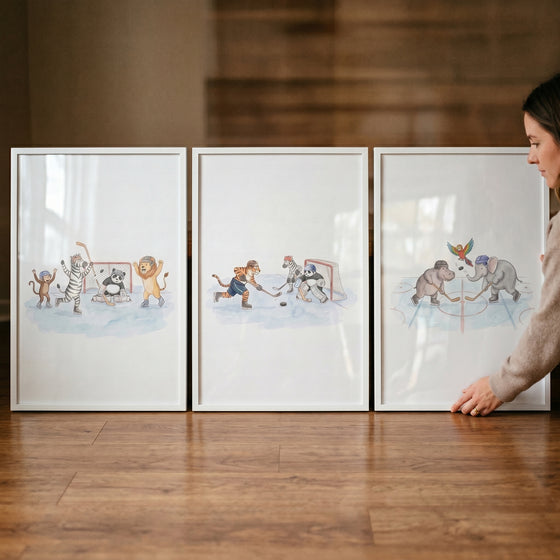 A woman touches a watercolor ice hockey animals wall art set of 3 in white frames resting on a wooden floor.