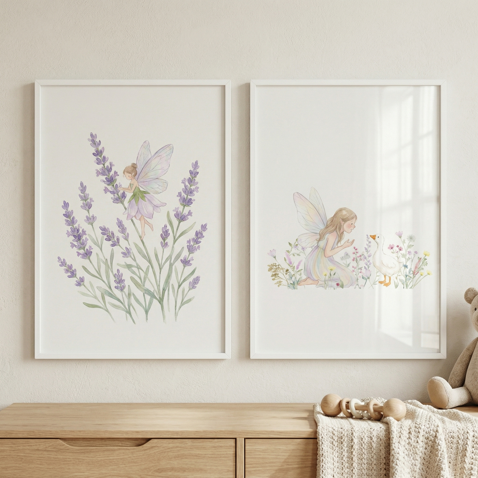 Two framed illustrations show delicate fairies with soft translucent wings one hovering among lavender stems and the other kneeling beside a small white duck surrounded by tiny flowers. The prints hang above a light wood dresser with a knitted blanket and wooden toy creating a gentle storybook nursery scene.