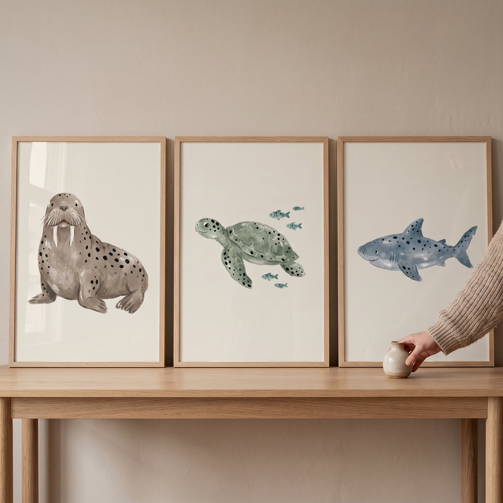 Framed watercolor neutral sea animals wall art set of 3 featuring a walrus, turtle, and shark on a wooden table.