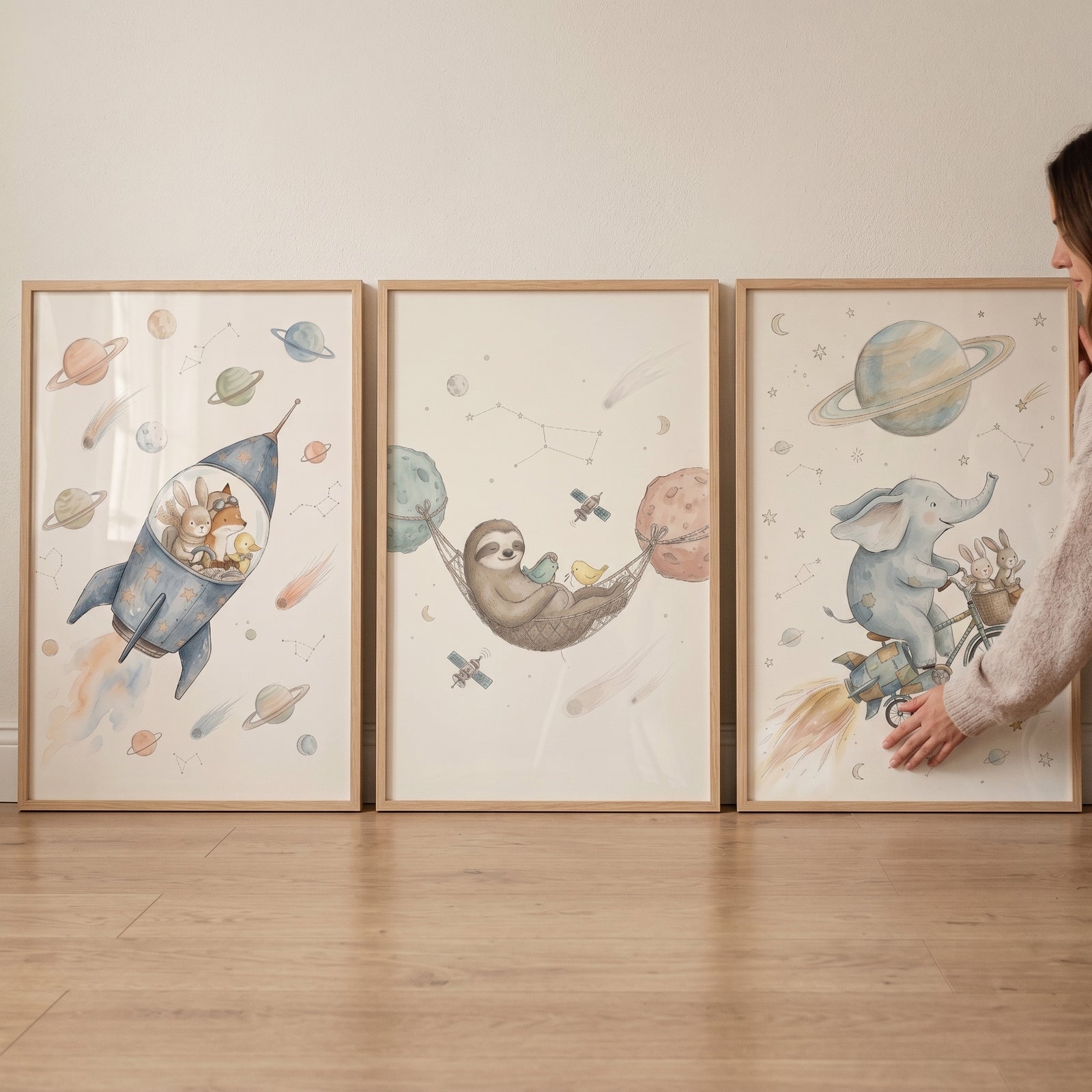 Watercolor neutral space animals wall art set of 3 featuring a rocket, a sloth in a hammock, and an elephant on a bike.