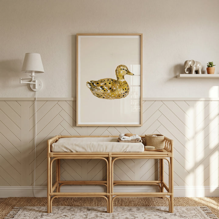Rattan changing table below watercolor ochre spotted duck wall art in a neutral nursery with chevron wall paneling.