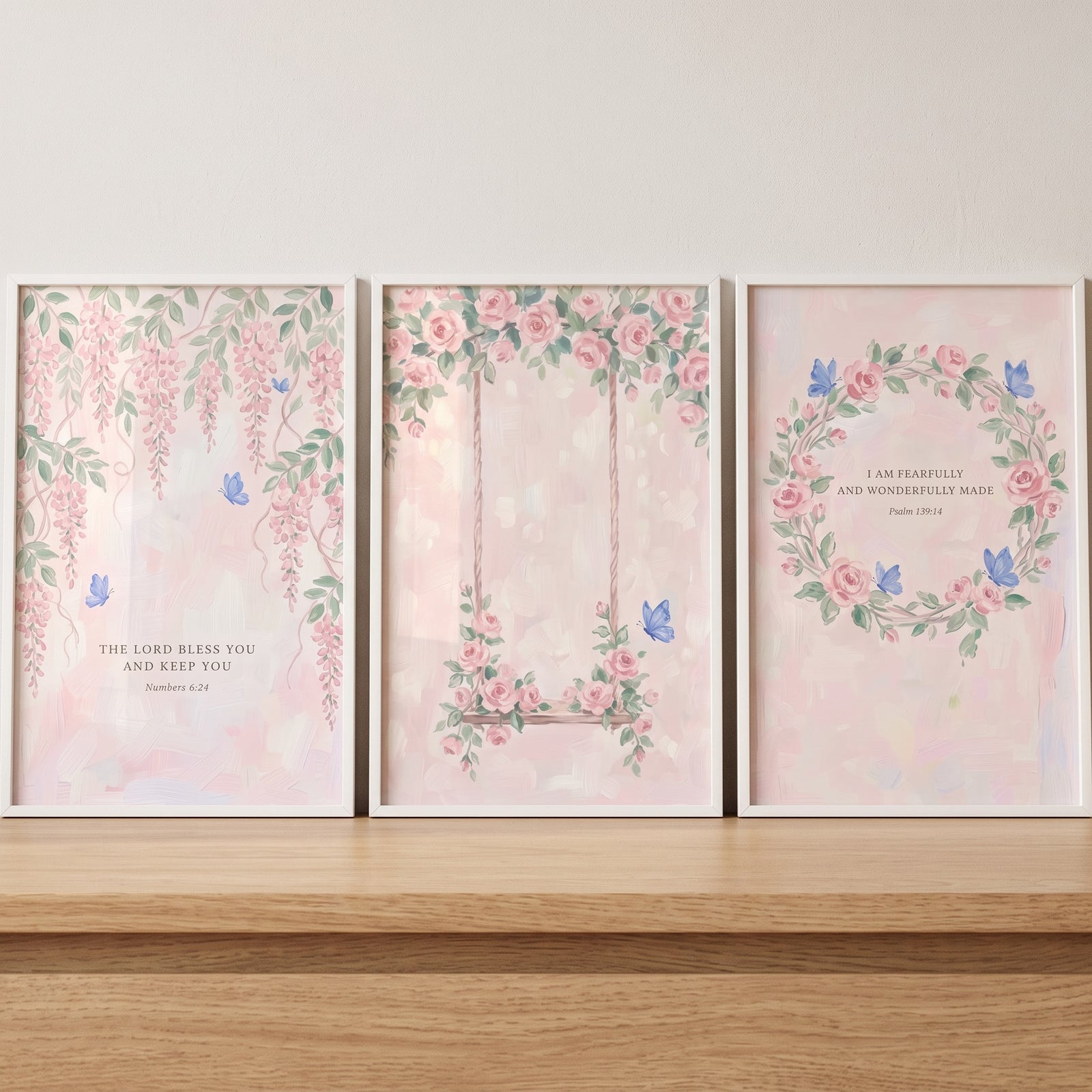 Watercolor pink floral scripture wall art set of 3 on a wooden shelf with wisteria, a swing, and a rose wreath.