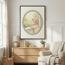 A well-lit room features white paneled walls and a large black-framed illustration of a cream-colored rabbit. The rabbit wears a floral bonnet and gazes out a window at a sunlit garden, framed by a green checkered scalloped oval. Beneath it, a light wood dresser holds books, a small lamp, and a potted plant. To the left is a window with sheer curtains and a basket of plush toys. To the right, an upholstered armchair is draped with a soft throw blanket.