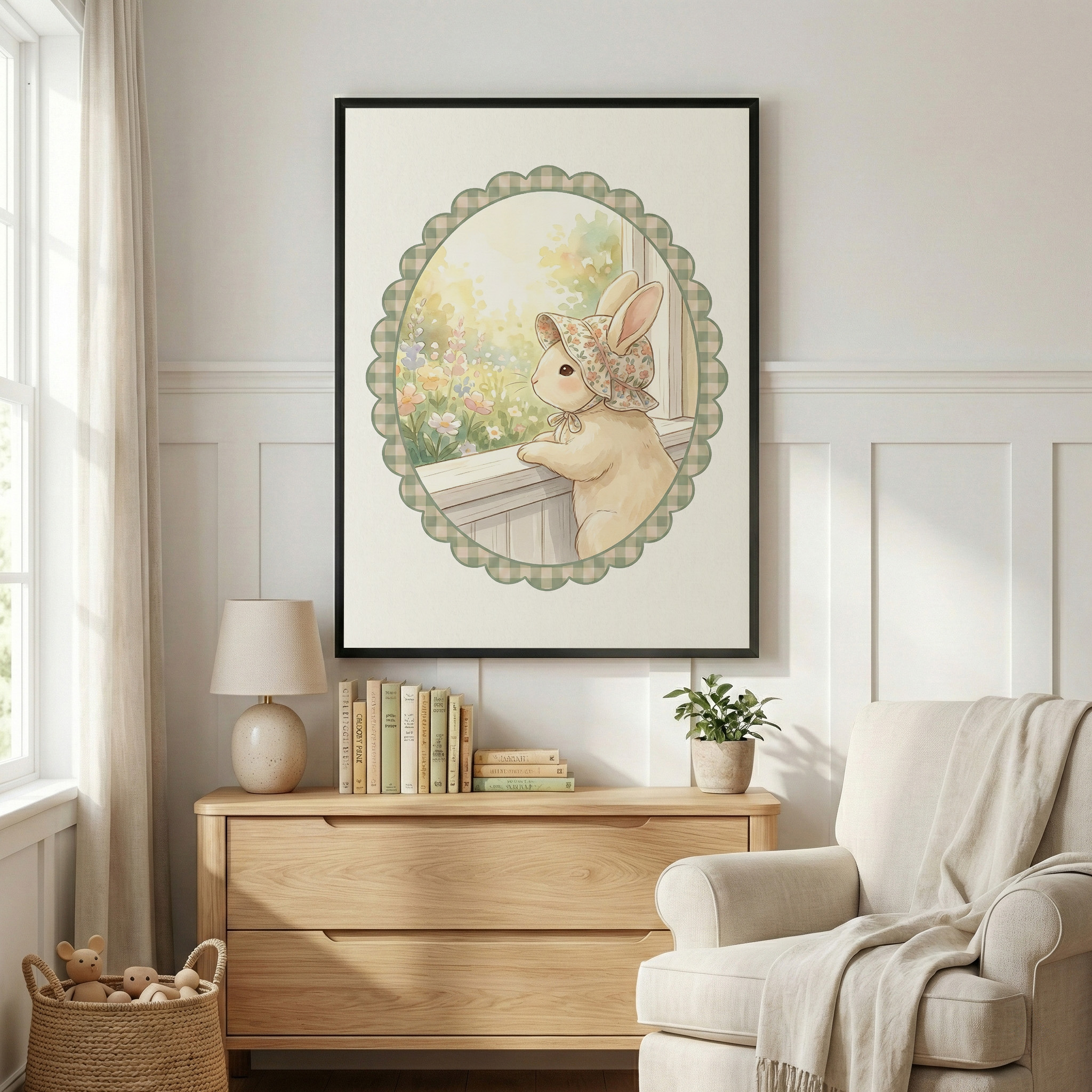 A well-lit room features white paneled walls and a large black-framed illustration of a cream-colored rabbit. The rabbit wears a floral bonnet and gazes out a window at a sunlit garden, framed by a green checkered scalloped oval. Beneath it, a light wood dresser holds books, a small lamp, and a potted plant. To the left is a window with sheer curtains and a basket of plush toys. To the right, an upholstered armchair is draped with a soft throw blanket.