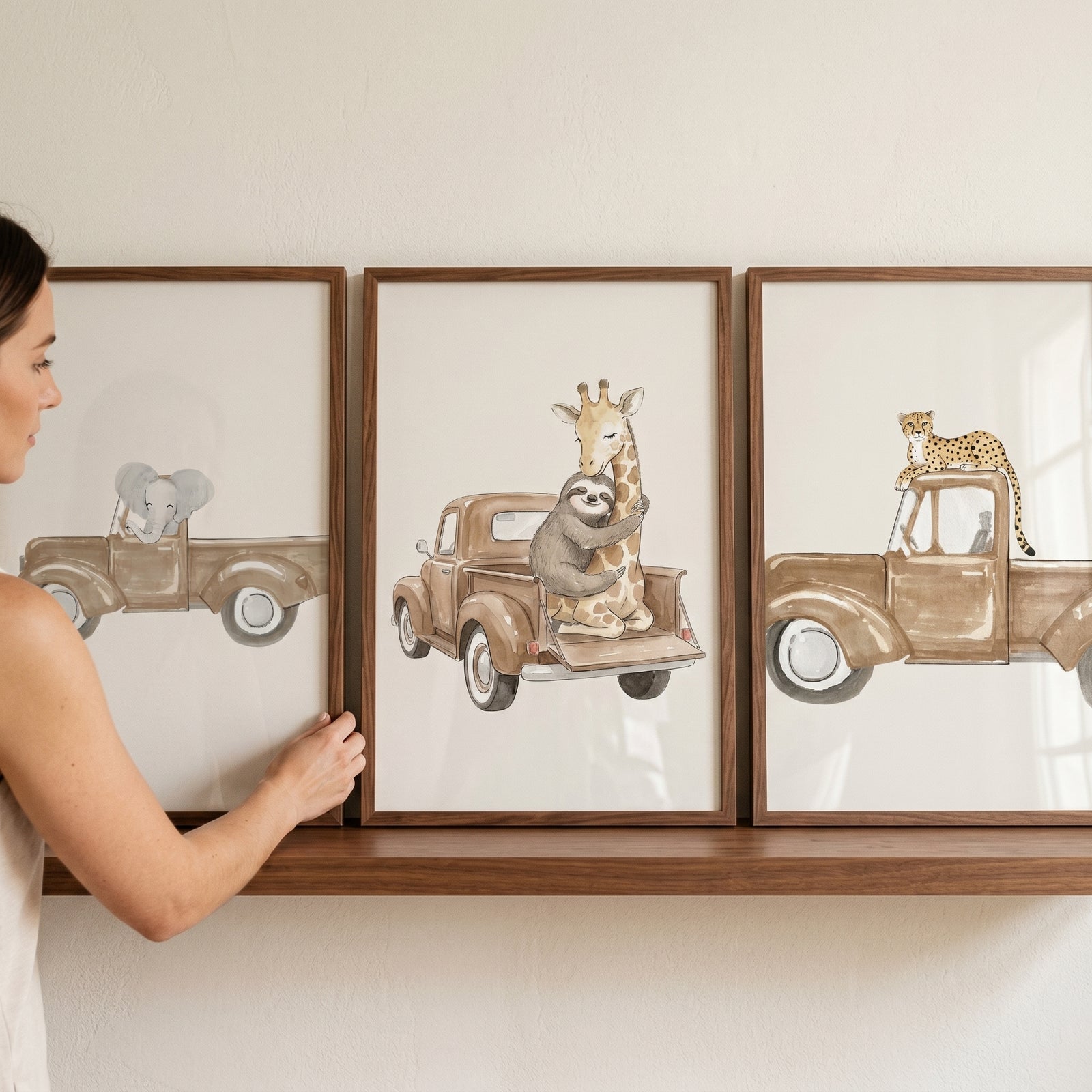 Woman adjusts a watercolor safari truck animals wall art set of 3 featuring an elephant, giraffe, sloth, and leopard.
