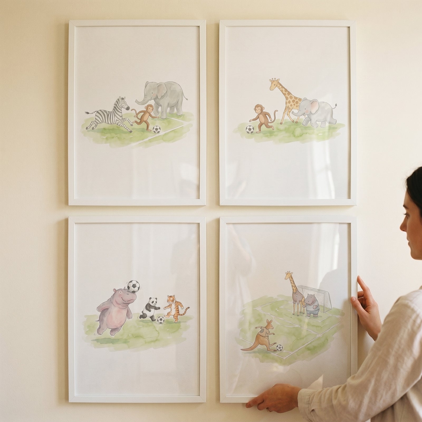 A woman hangs a watercolor soccer safari animals wall art set of 4 featuring animals like giraffes and zebras.