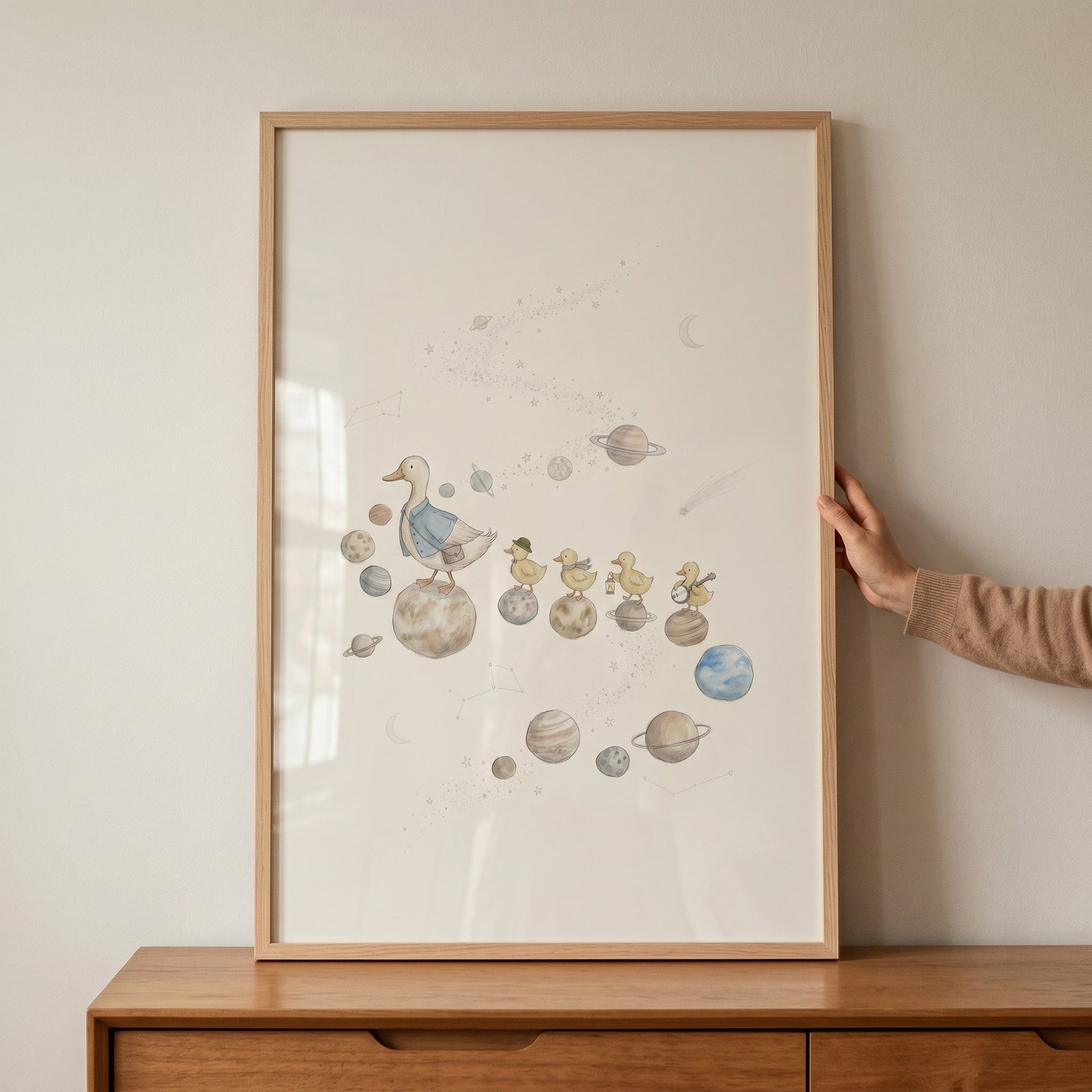 Watercolor space walking duck wall art showing ducks on planets, framed and resting on a wooden dresser.
