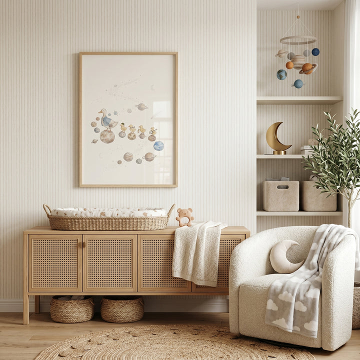 Nursery with watercolor space walking duck wall art, a rattan sideboard, and a white armchair with moon accents.