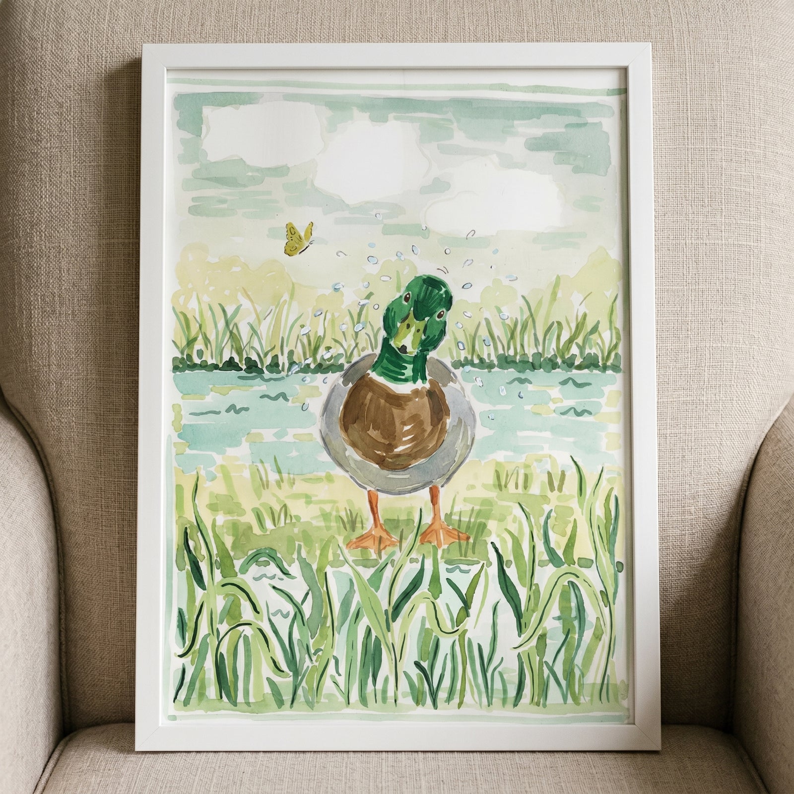 Watercolor splashing mallard duck wall art shows a green-headed duck shaking off water in grass with a yellow butterfly.