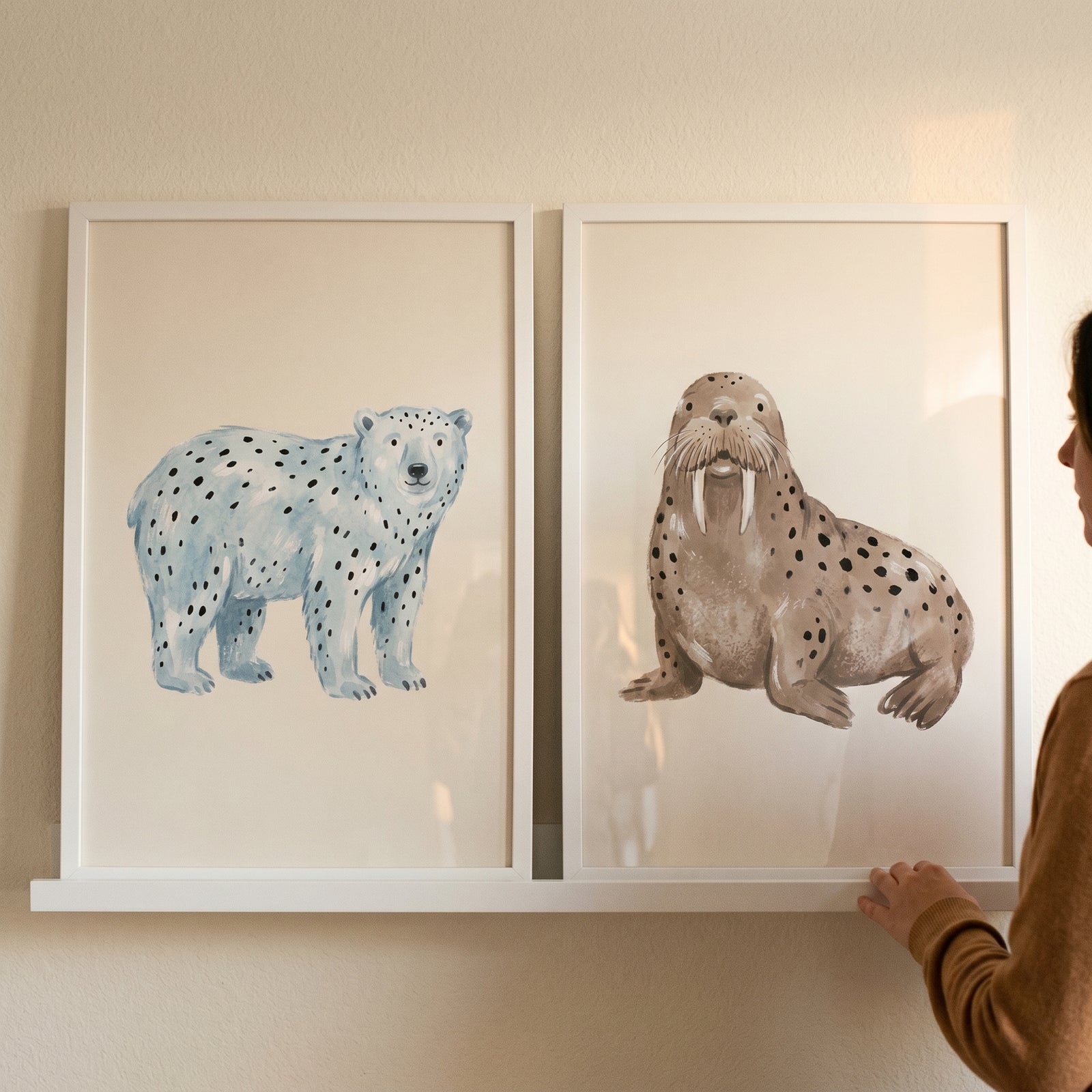 Watercolor spotted arctic animals wall art set of 2 featuring a polar bear and walrus in white frames on a shelf.