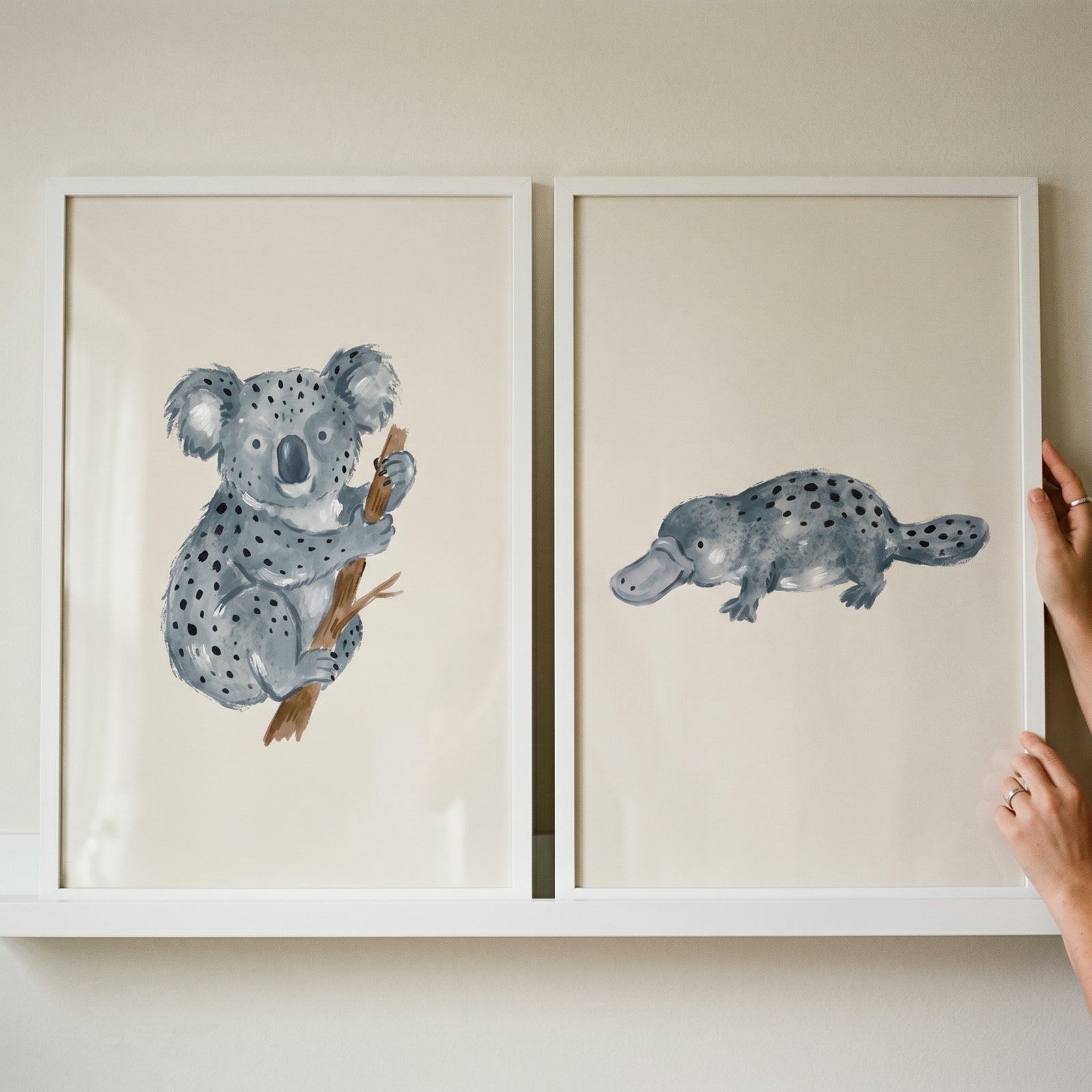 Watercolor spotted Australian animals wall art set of 2 featuring a koala and a platypus in white frames on a shelf.