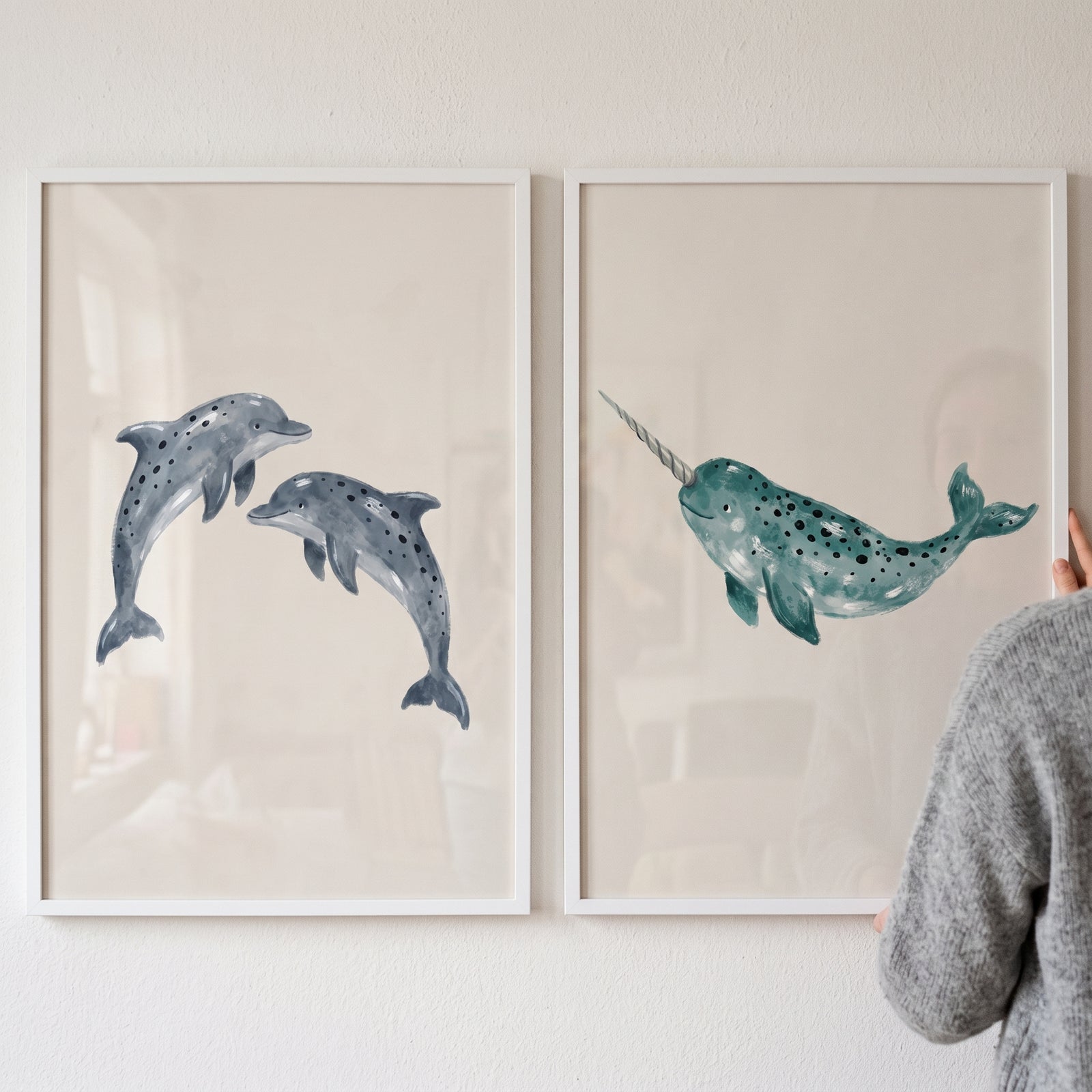 Watercolor spotted marine animal wall art set of 2 featuring two dolphins and a narwhal in white frames.