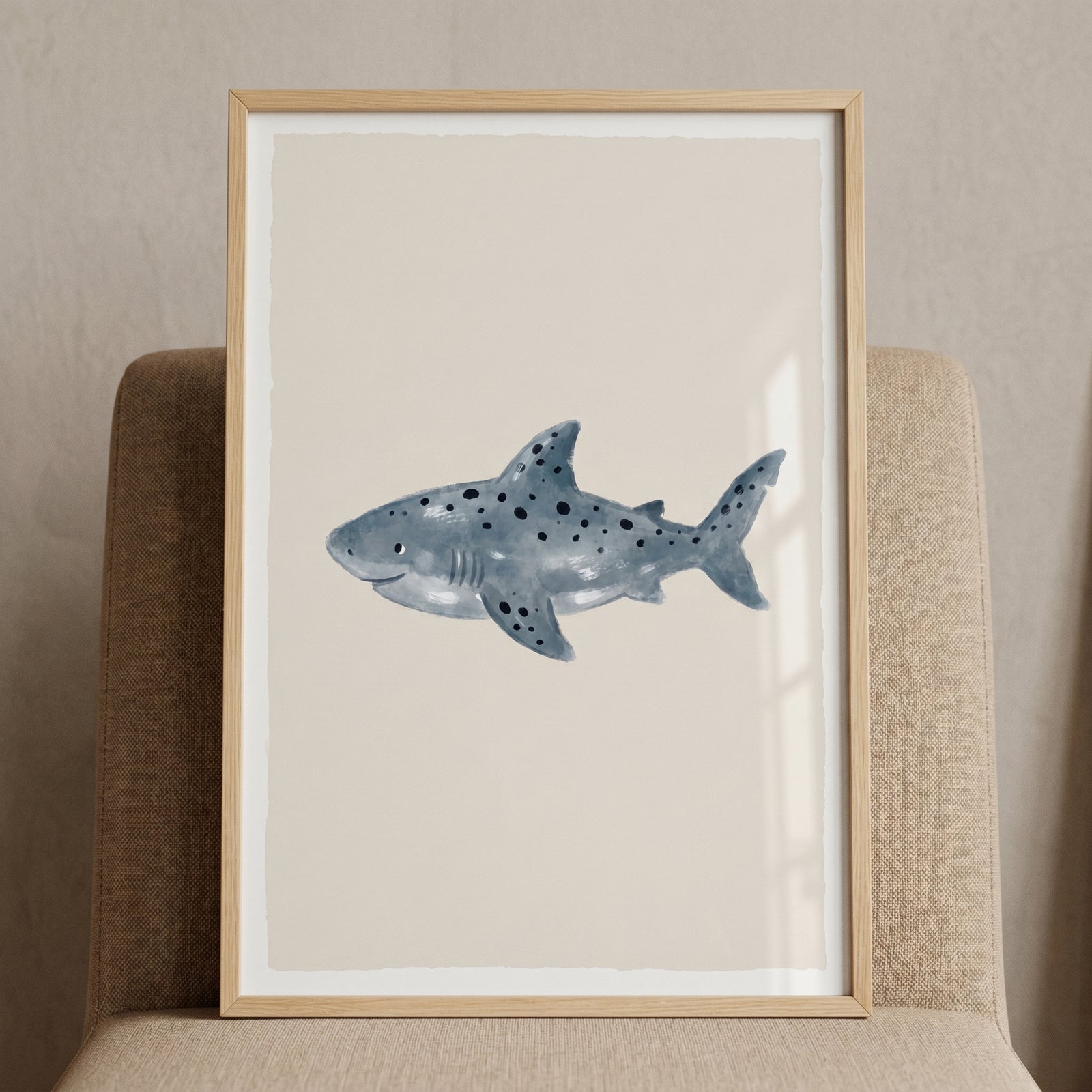 Watercolor spotted shark wall art in a light wood frame, resting on a beige chair against a neutral background.