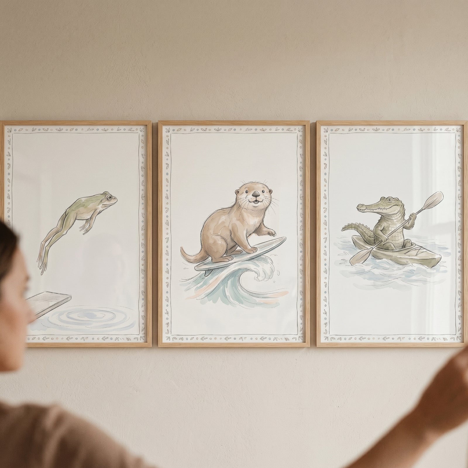 Watercolor water sports animals wall art set of 3 featuring a jumping frog, a surfing otter, and a kayaking crocodile.