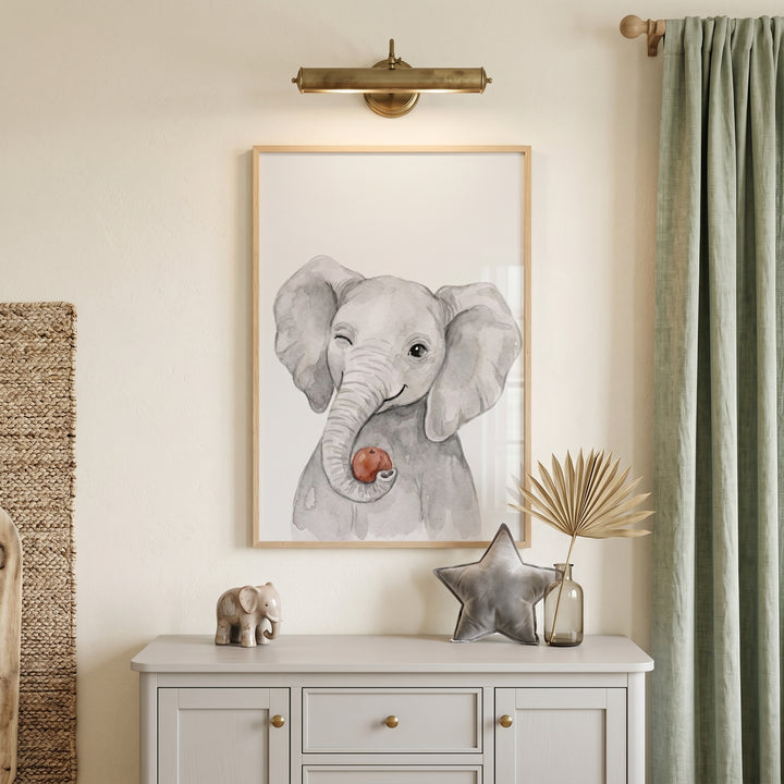 Watercolor winking elephant wall art above a grey dresser with a star pillow and figurine. Sage green curtains are nearby.