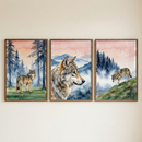 Three framed watercolor-style illustrations hang side-by-side. The left artwork depicts a wolf standing in a blue-toned forest under a pink sky. The center piece features a large close-up profile of a wolf's head with misty blue mountains in the background. The right artwork shows a wolf walking down a grassy slope with a misty forest behind it. The scenes are tied together by a consistent color palette of soft pinks, blues, and natural tones.