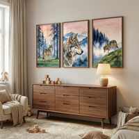 A wide-angle, eye-level indoor shot shows three large, vertical framed pieces of watercolor-style artwork of wolves in a natural setting hanging above a mid-century modern wooden dresser. The artwork features wolves in various poses—one standing in a forest, another in a close-up profile, and a third walking on a grassy hill—all set against a backdrop of soft pink and blue mountains. The dresser is a rich brown wood with nine drawers and sits on a plush, cream-colored rug. 