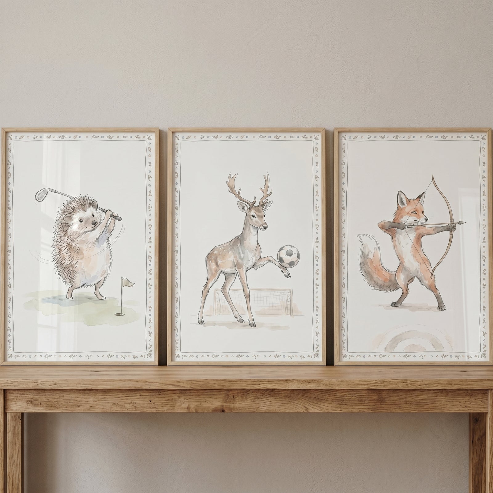 Watercolor woodland sports animals wall art set of 3 with a golfing hedgehog, soccer deer, and archer fox on a wooden table.