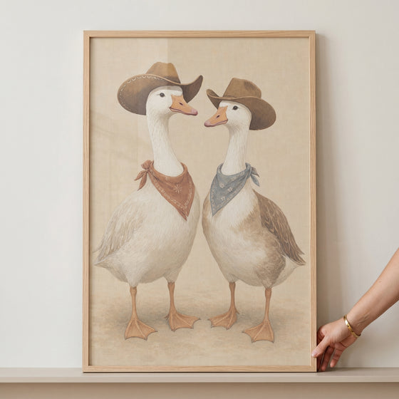 Western cowboy duo geese wall art featuring two geese in brown hats and bandanas, presented in a light wood frame.