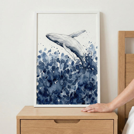 Framed watercolor painting of a whale breaching from a sea of abstract navy and blue brushstrokes, suggesting ocean waves. The minimalist style and fluid water textures create a calm, nature-inspired aesthetic.