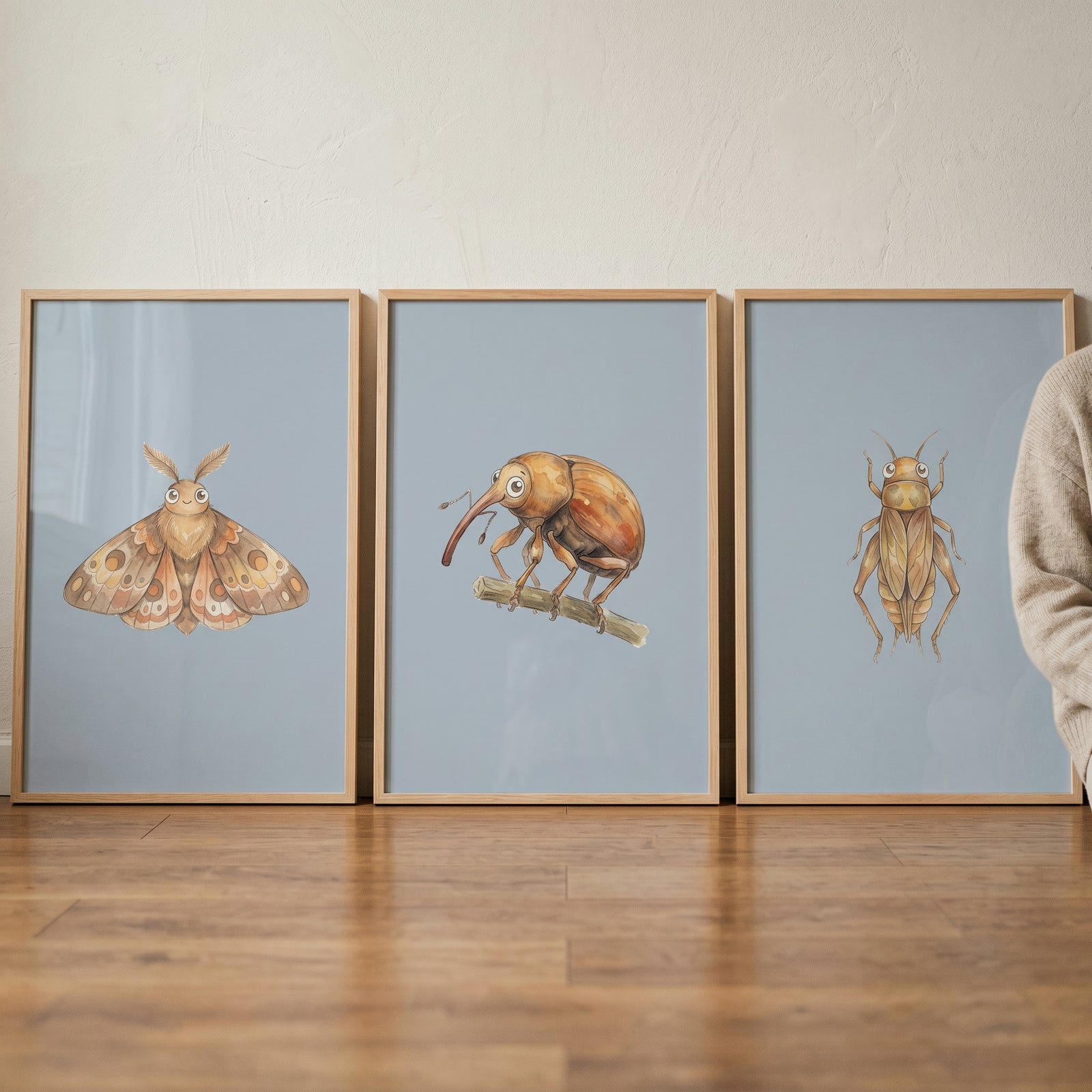 Whimsical blue bug artwork set of 3 featuring a moth, weevil, and cricket in wooden frames resting on a floor.