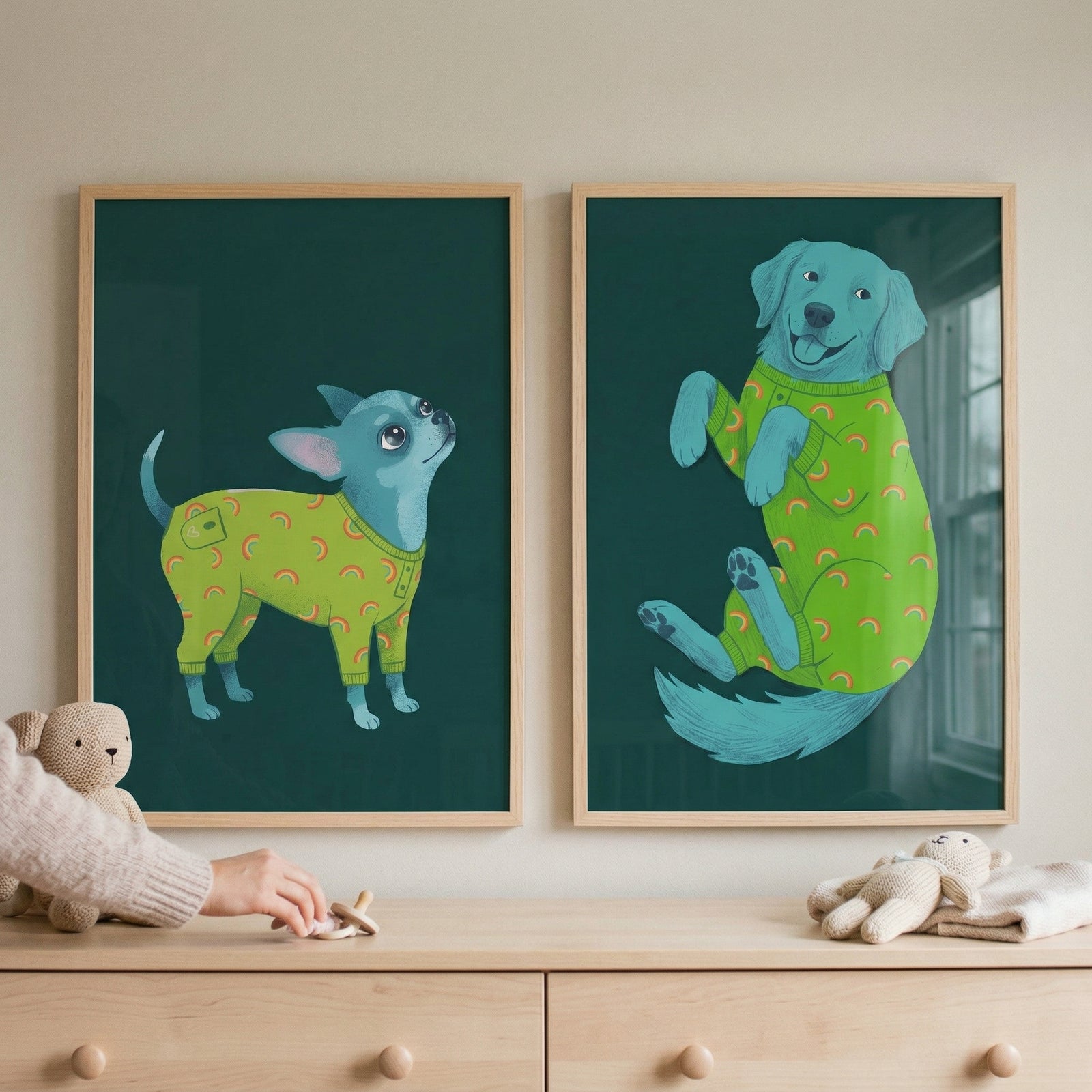 Two framed illustrations hang side-by-side on a light-colored wall above a light wood dresser. On the left, a small, stylized blue dog stands and looks upward, wearing lime green pajamas decorated with small orange rainbows. 