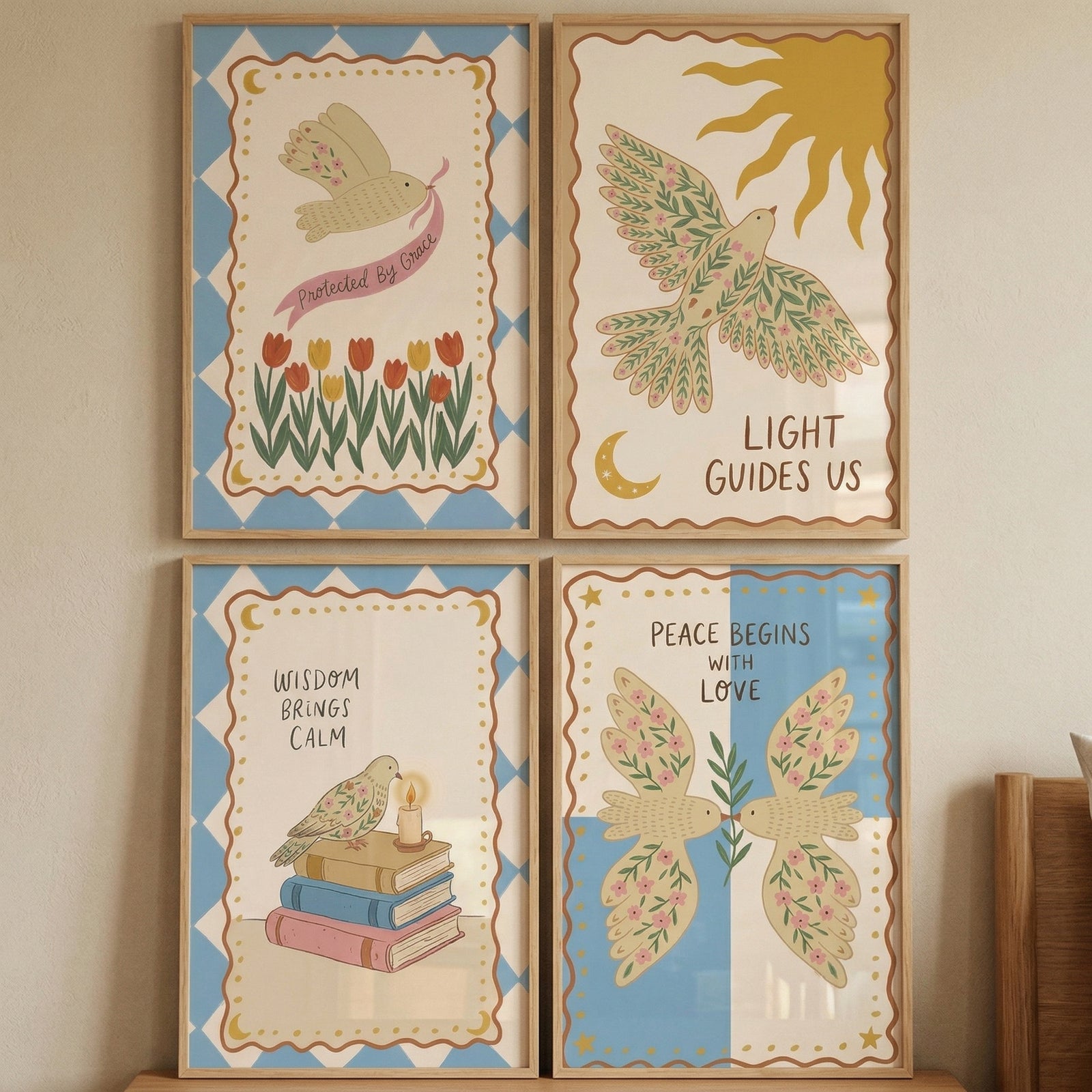 Four framed illustrations are arranged in a square grid on a neutral wall. Each features a cream-colored bird with floral wing patterns and an inspirational quote. The top-left shows a bird with a pink ribbon over tulips. 