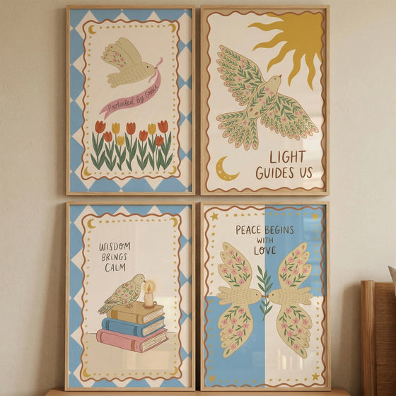 Four framed illustrations are arranged in a square grid on a neutral wall. Each features a cream-colored bird with floral wing patterns and an inspirational quote. The top-left shows a bird with a pink ribbon over tulips. 