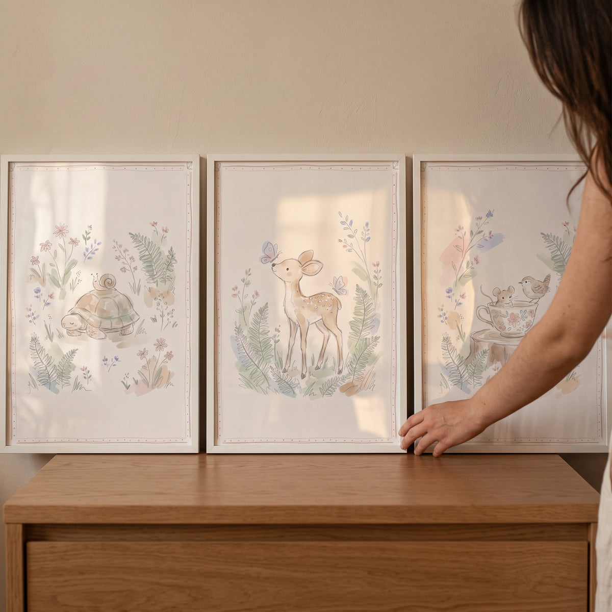 A person arranges a whimsical botanical forest animal wall art set of 3 featuring a turtle, deer, and mouse on a wood.